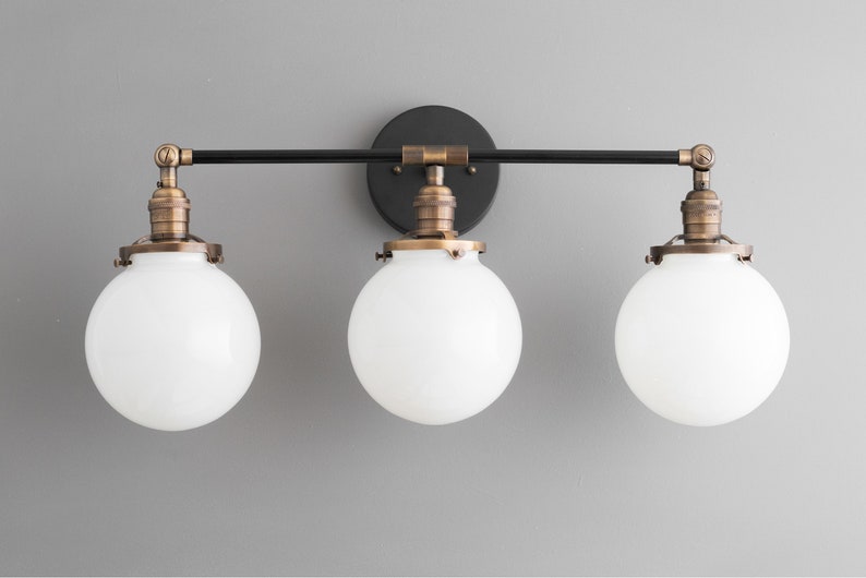 May include: A three-light vanity fixture with a black metal frame and white glass globes. The fixture has a brushed brass finish.