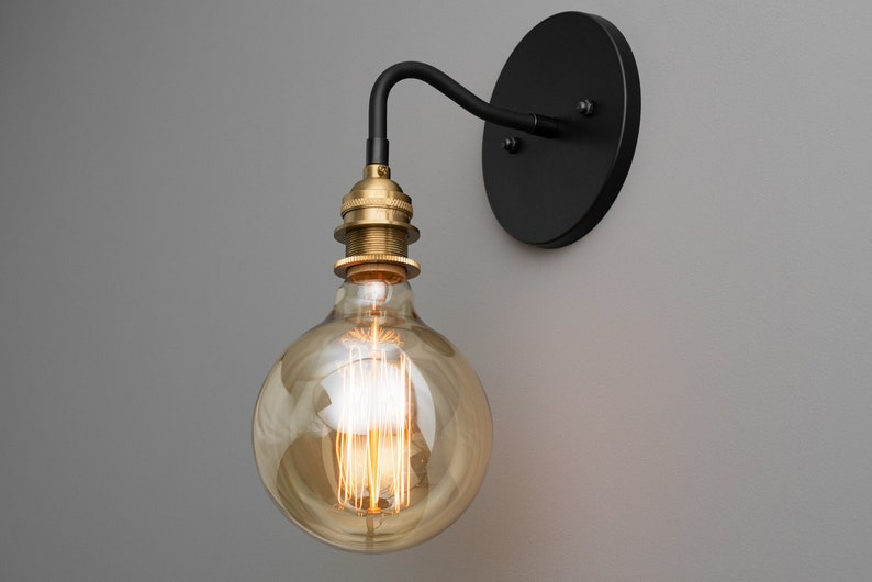 K&ouml;nnte beinhalten: Eine schwarze Wandleuchte mit einer Messingfassung und einer klaren Gl&uuml;hbirne. Die Gl&uuml;hbirne ist eine Gl&uuml;hbirne mit Vintage-Filament.