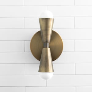 May include: A brass wall sconce with two light bulbs. The sconce has a round base and two cone-shaped shades.