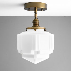 Puede incluir: Una l&aacute;mpara de techo de vidrio blanco con acabado en lat&oacute;n. La luz tiene un dise&ntilde;o geom&eacute;trico y est&aacute; suspendida de una cubierta redonda de lat&oacute;n.