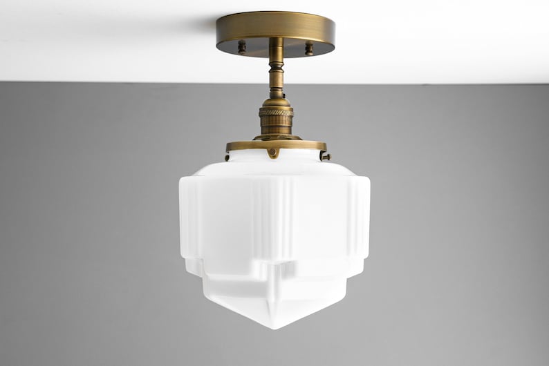 Puede incluir: Una l&aacute;mpara de techo de vidrio blanco con acabado en lat&oacute;n. La luz tiene un dise&ntilde;o geom&eacute;trico y est&aacute; suspendida de una cubierta redonda de lat&oacute;n.