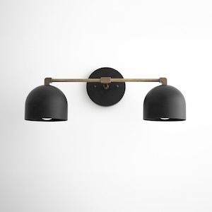 May include: Black wall sconce with two black dome-shaped shades and a brass arm.