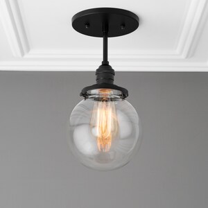 May include: A black ceiling light fixture with a clear glass globe shade and a single light bulb.