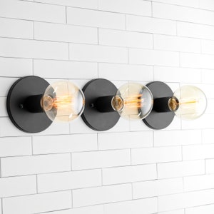May include: A modern light fixture with four round, clear glass bulbs. Each bulb is attached to a black circular base. The fixture is mounted on a white tiled wall, creating a minimalist aesthetic.