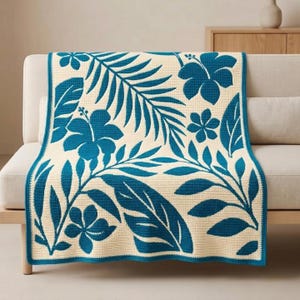 May include: A rectangular crochet blanket featuring a cream-colored base with a repeating pattern of dark teal hibiscus flowers and tropical palm leaves. The textile has a visible woven texture and a solid dark teal border along the edges.