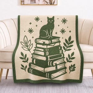 Könnte beinhalten: Eine cremefarbene Häkeldecke mit dunkelgrünem Rand, die in der Mitte ein Motiv einer Katze auf einem Stapel aus fünf Büchern zeigt, umgeben von stilisierten Blattzweigen und Sternenmustern, alles in dunkelgrünem Garn gearbeitet.