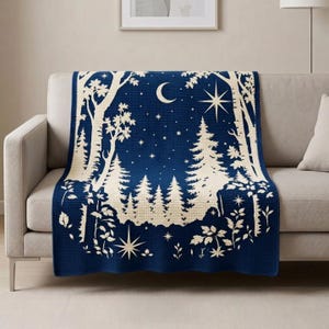 May include: A dark blue woven throw blanket featuring a cream-coloured forest scene with tall pine trees, deciduous trees, and leafy plants. The night sky design includes a crescent moon and various star shapes scattered across the upper section.
