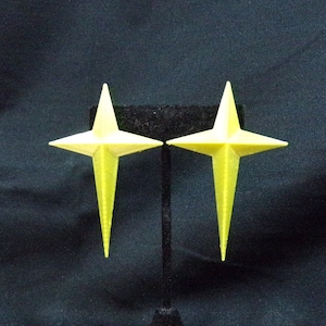 May include: A pair of yellow star-shaped earrings on a black display stand.