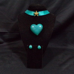 May include: Teal heart-shaped pendant necklace with matching earrings and a gold star charm on a teal ribbon choker.