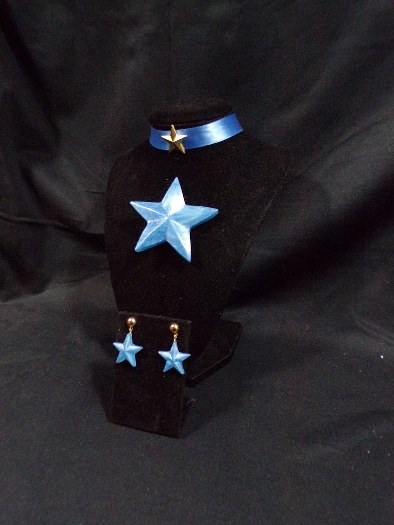 May include: A blue star-shaped pendant necklace with a gold star charm and matching blue star earrings. The jewellery is displayed on a black velvet stand.