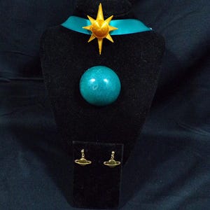 Pode incluir: Um colar com um orbe azul turquesa e um pingente de estrela dourada, e brincos combinando com um orbe azul turquesa e an&eacute;is de Saturno dourados.