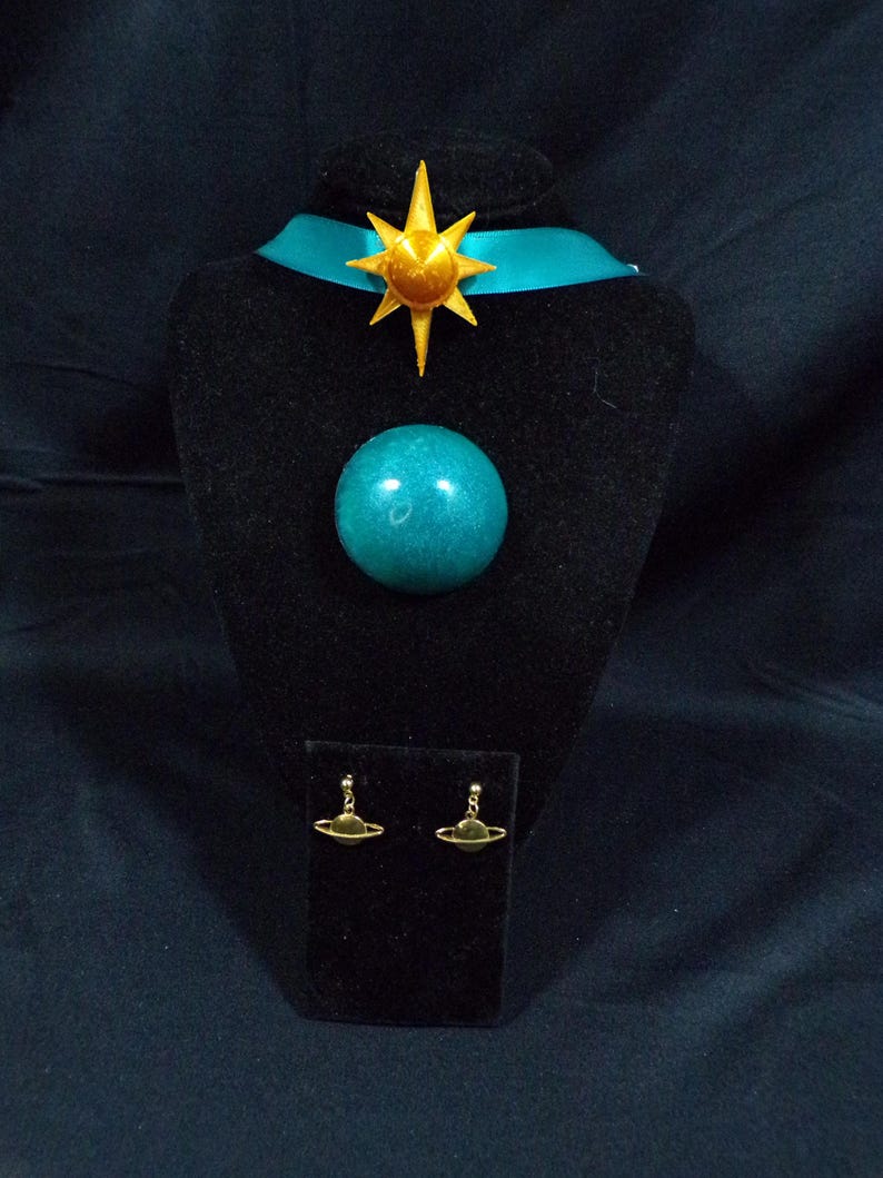 Pode incluir: Um colar com um orbe azul turquesa e um pingente de estrela dourada, e brincos combinando com um orbe azul turquesa e an&eacute;is de Saturno dourados.
