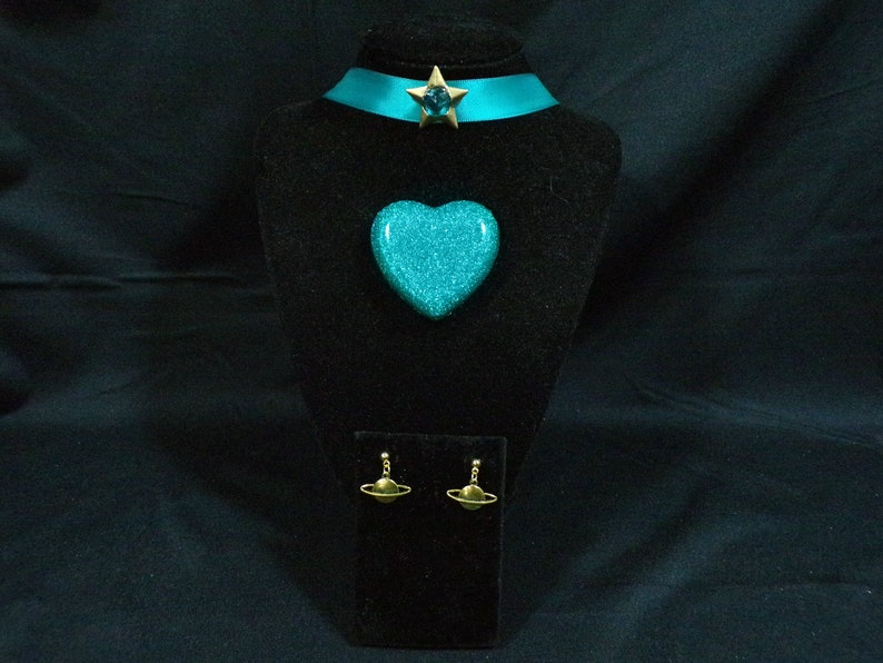 May include: A turquoise blue heart-shaped pendant necklace with a gold star charm and matching turquoise blue earrings with gold planet charms.
