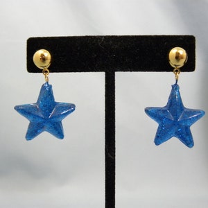 May include: A pair of blue glitter star earrings with gold posts and backs.