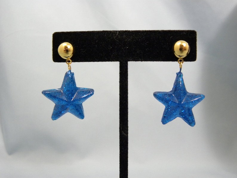 May include: A pair of blue glitter star earrings with gold posts and backs.