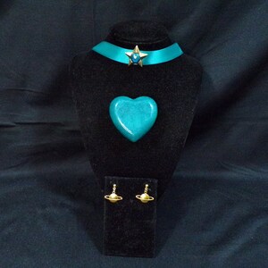 May include: Teal blue heart-shaped pendant, teal blue choker with a gold star charm, and gold earrings with a ring design.