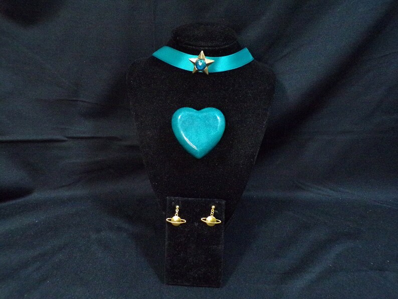 May include: Teal blue heart-shaped pendant, teal blue choker with a gold star charm, and gold earrings with a ring design.