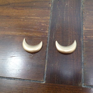 May include: Two gold crescent moon shaped earrings on a wooden surface.