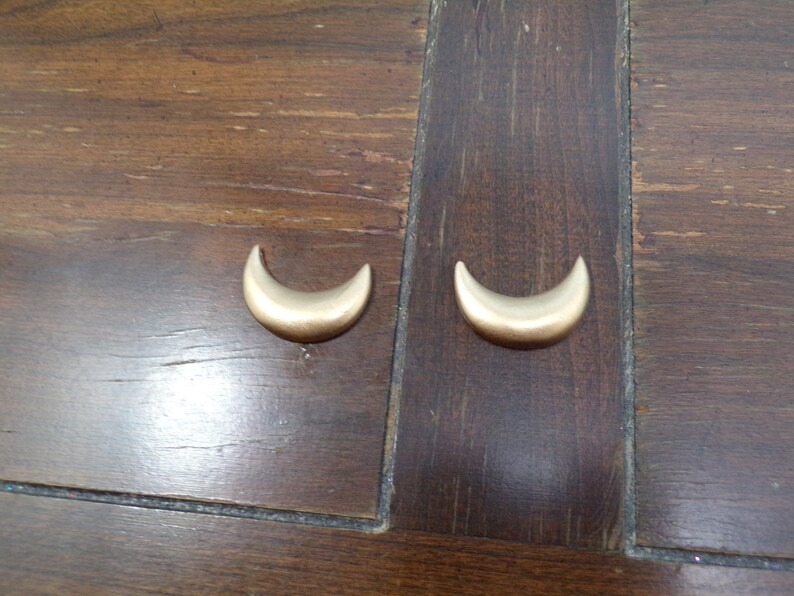 May include: Two gold crescent moon shaped earrings on a wooden surface.