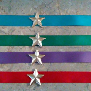 May include: Four satin ribbon strips with silver star embellishments. The ribbons are turquoise, green, purple, and red.
