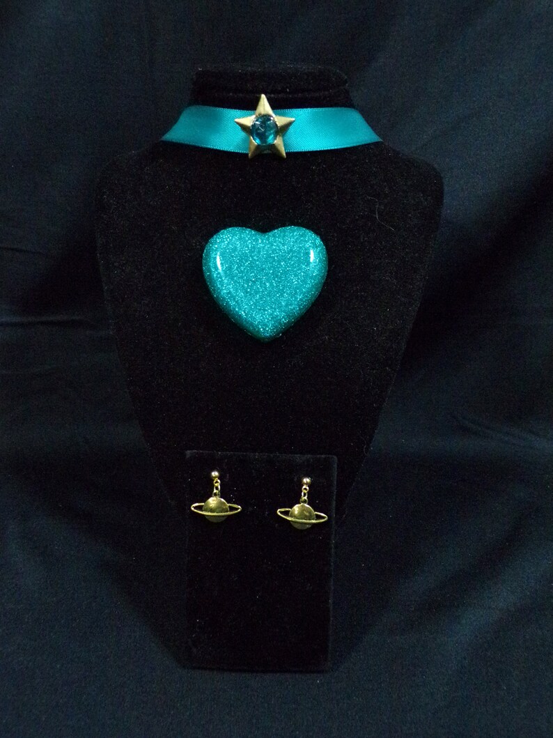 May include: A turquoise glitter heart pendant necklace with a gold star charm and matching turquoise glitter earrings with gold planet charms.