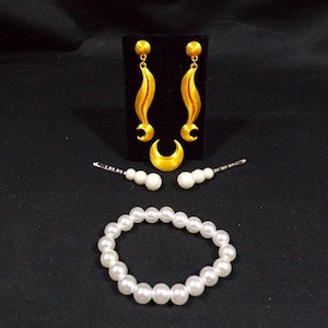 May include: A set of gold earrings with a crescent moon design, two white pearl hair clips, and a white pearl necklace.