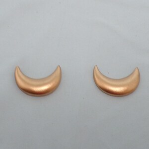 May include: A pair of gold crescent moon earrings. The earrings are made of a smooth, shiny metal.