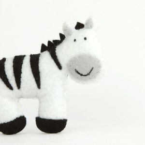 May include: A white and black stuffed zebra toy with a smiling face. The zebra is made of felt and has a soft, cuddly texture.