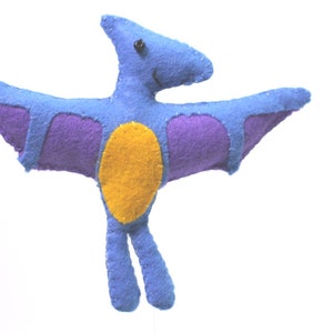 May include: A blue felt pterodactyl toy with purple wings and a yellow belly. The toy has a black button eye and a stitched smile.