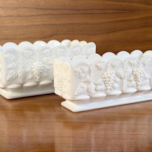 Op de afbeelding: Twee rechthoekige plantenbakken van wit melkglas met een reliëfpatroon van druiventrossen en bladeren. Elke bak heeft een geschulpte bovenrand en een stevige voet, met een consistente ondoorzichtige afwerking en gedetailleerde botanische motieven.
