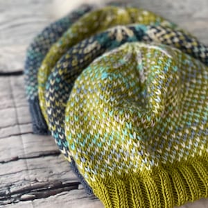 以下が含まれることがあります： ポンポンが付いたニット帽が3つ。帽子は緑、青、白で、斑点模様になっています。帽子は重ねられています。