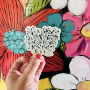 May include: A white sticker with black calligraphy that reads "She is clothed in strength and dignity and she laughs without fear of the future."
