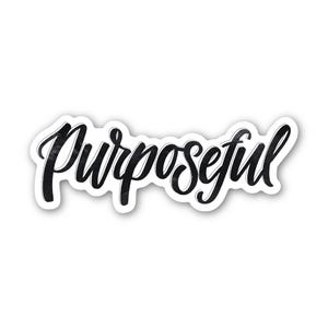 May include: A white sticker with the word "Purposeful" in black, handwritten-style script. The word has a slight textured effect, and the sticker has a white border.