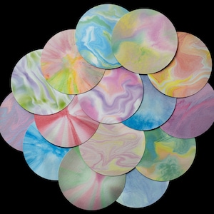 May include: A collection of 12 round paper discs with marbled patterns in shades of blue, pink, yellow, and green. The discs are arranged in a circular pattern, with the largest disc in the center and the smallest discs on the outside.