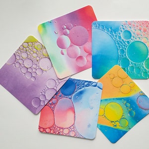 May include: Six colorful coasters with abstract designs featuring colorful circles and swirls. The coasters are made of a durable material and are perfect for protecting your furniture from spills and scratches.