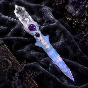 May include: A decorative dagger featuring a clear, faceted quartz crystal blade and a handle adorned with sculpted white vines, light blue leaves, and two round, polished purple amethyst spheres set into the center of the hilt.