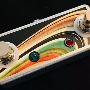 以下が含まれることがあります： 2つのボタンと2つのLEDライトが付いたシルバーのフットペダル。ペダルは、黒、白、緑、オレンジ、赤の色を使用したカラフルな抽象的なデザインです。