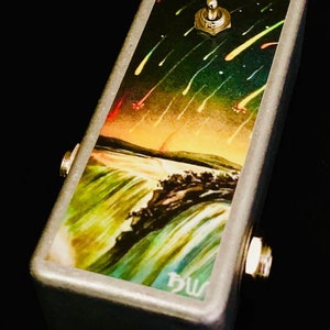 May include: A silver effect pedal with a black and green design featuring a waterfall and shooting stars. The pedal has a toggle switch and two input jacks. The text "bw" is printed on the pedal.