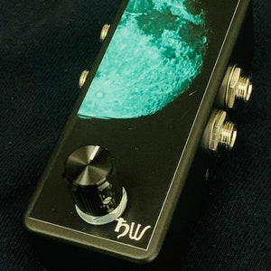 May include: Black guitar effects pedal with a green moon graphic, a single knob, and two input and output jacks. The pedal is labelled "hw".