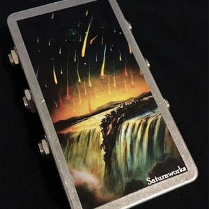 May include: A rectangular, silver-framed effects pedal with a colourful graphic. The graphic depicts a waterfall scene under a night sky with falling streaks of light. The text "Saturnworks" is visible on the bottom right.