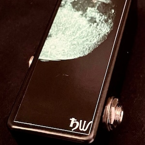 May include: Black guitar effects pedal with a moon graphic and a green button. The pedal has a white "hw" logo on the bottom.