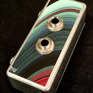 May include: A silver metal pedal with a black and green swirl design. The pedal has two 1/4 inch jacks and the text "bw" on the side.
