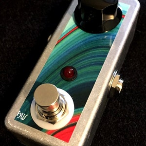May include: A silver effect guitar pedal with a green, blue, and red swirl design. The pedal has a single footswitch, a knob, and a red LED.