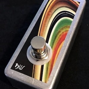 May include: A silver stompbox with a colourful graphic of a rainbow design. The stompbox has a single footswitch with a white button and a black label with the text "bw".