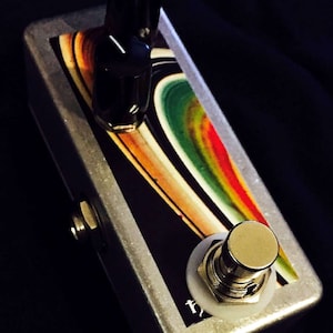 May include: A silver effects pedal with two black knobs and a white footswitch. The pedal has a colorful abstract design on the top.
