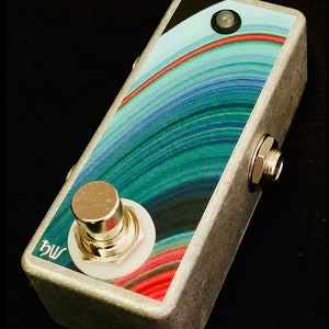 May include: A silver effect pedal with a blue, green, and red abstract design. The pedal has a single footswitch with a white button and a silver knob. The text "bw" is printed on the pedal.
