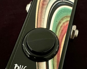 Puede incluir: Pedal negro con un botón negro grande y un diseño abstracto colorido. El pedal tiene las letras "bw" impresas en él.