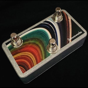 May include: A silver stompbox with three footswitches and a colorful abstract design. The text "Saturnworks" is printed on the side of the box.