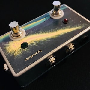 May include: A silver effect pedal with two footswitches, a green LED, a red LED, and two 1/4 inch jacks. The pedal has a graphic of a comet on a dark blue background with the text "Saturnworks" printed on the side.
