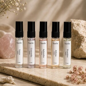 May include: Five clear glass spray bottles with black caps, each containing 5 mL of liquid. Labels read huele, Velixir, and the names Icarus, Concordia, Aphrodite, Athena, and Poseidon. The liquids are clear, light purple, light pink, gold, and light green.